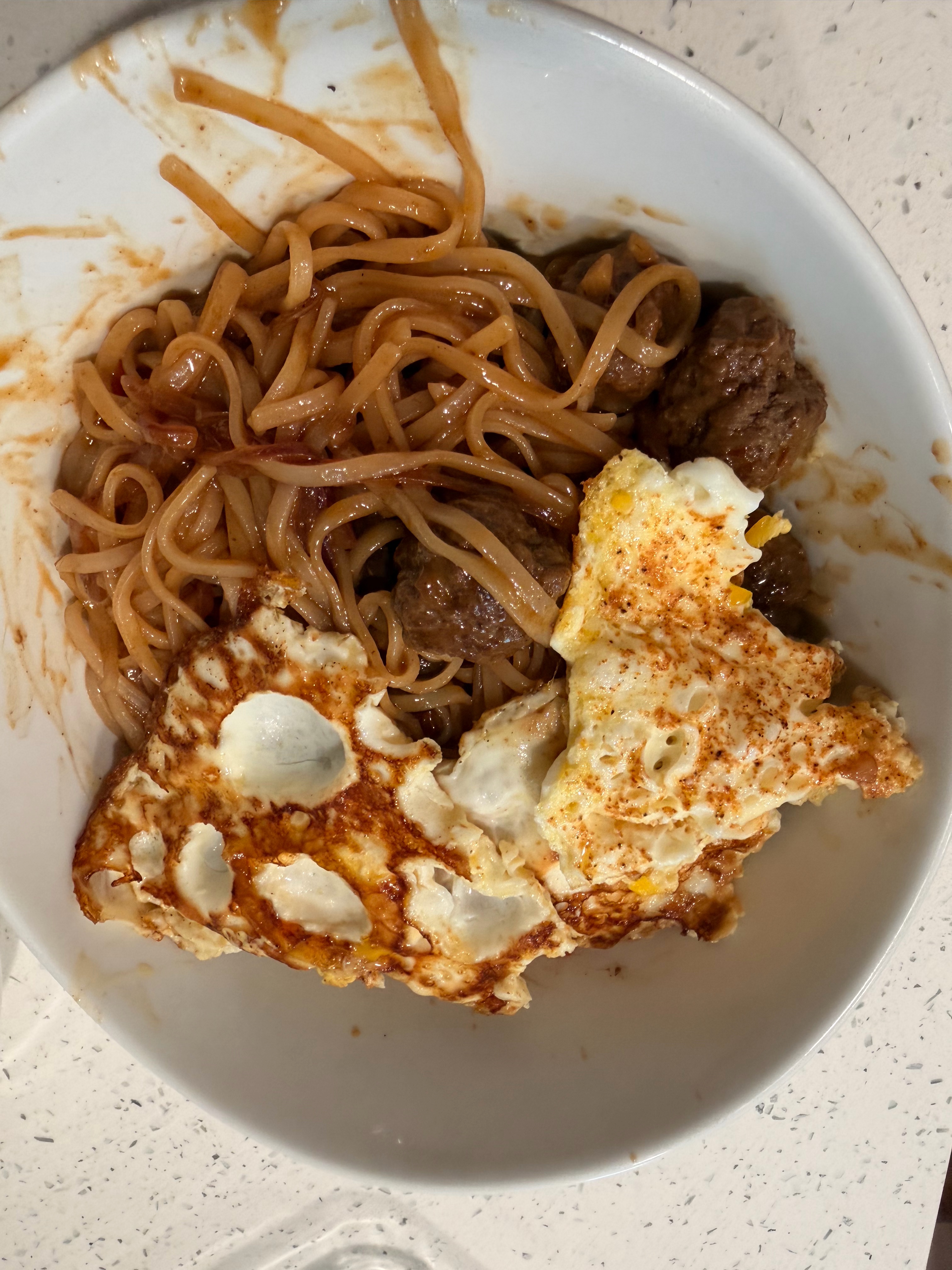 A bowl of Asian spaghetti with noodles, tiny meatballs, and two fried eggs on top